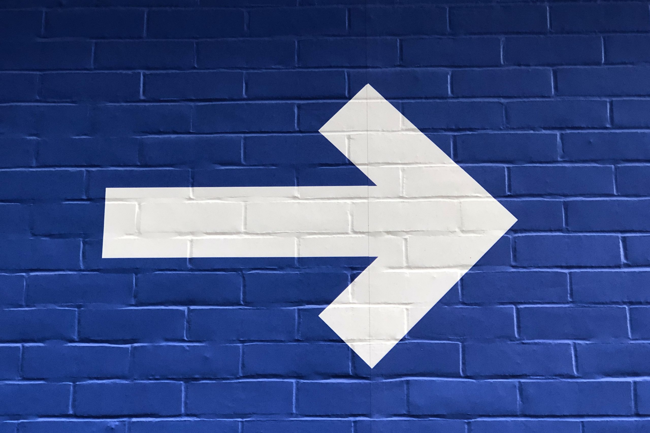 Blue brick wall with a large white arrow pointing right