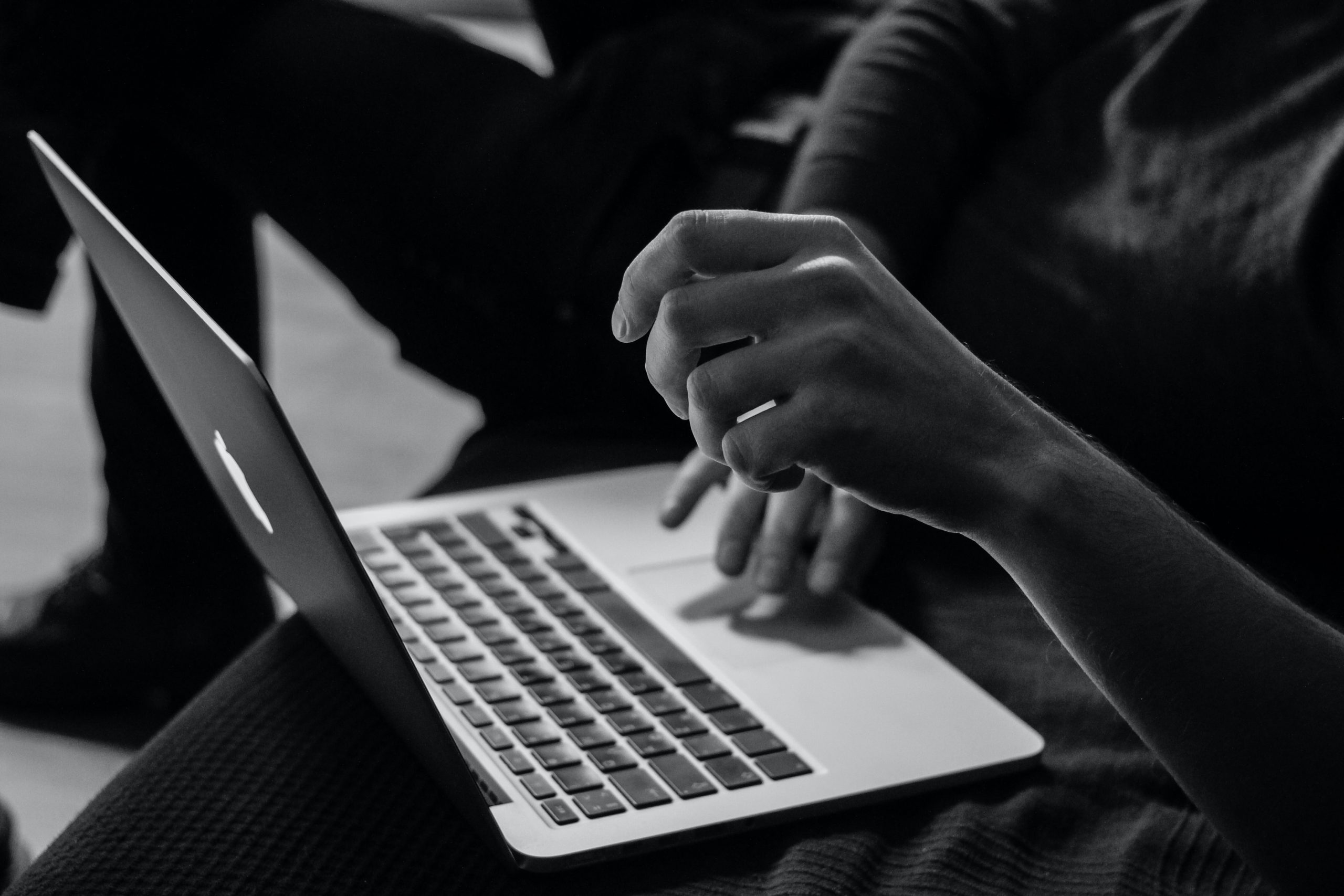 Black and white photo of hands using a laptop trackpad